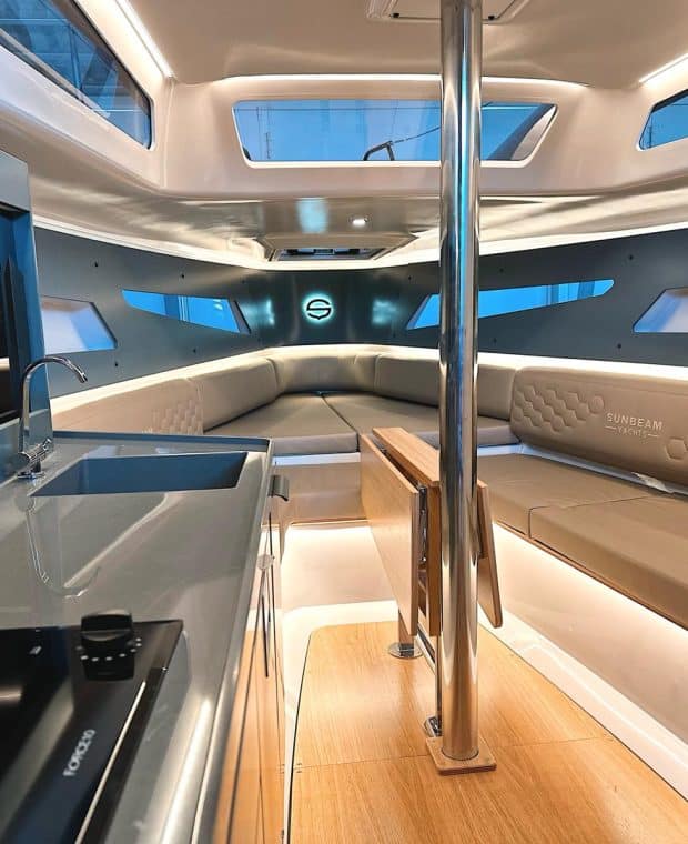 Weitwinkel-Innenansicht der SUNBEAM 32.1 Yacht zeigt die geräumige Kajüte mit Sitzgelegenheiten, Küchenbereich und zahlreichen Fenstern für natürliches Licht.