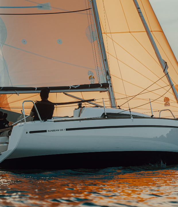 Segler genießt einen malerischen Sonnenuntergang auf einer Sunbeam Yacht mit orangefarbenen Segeln