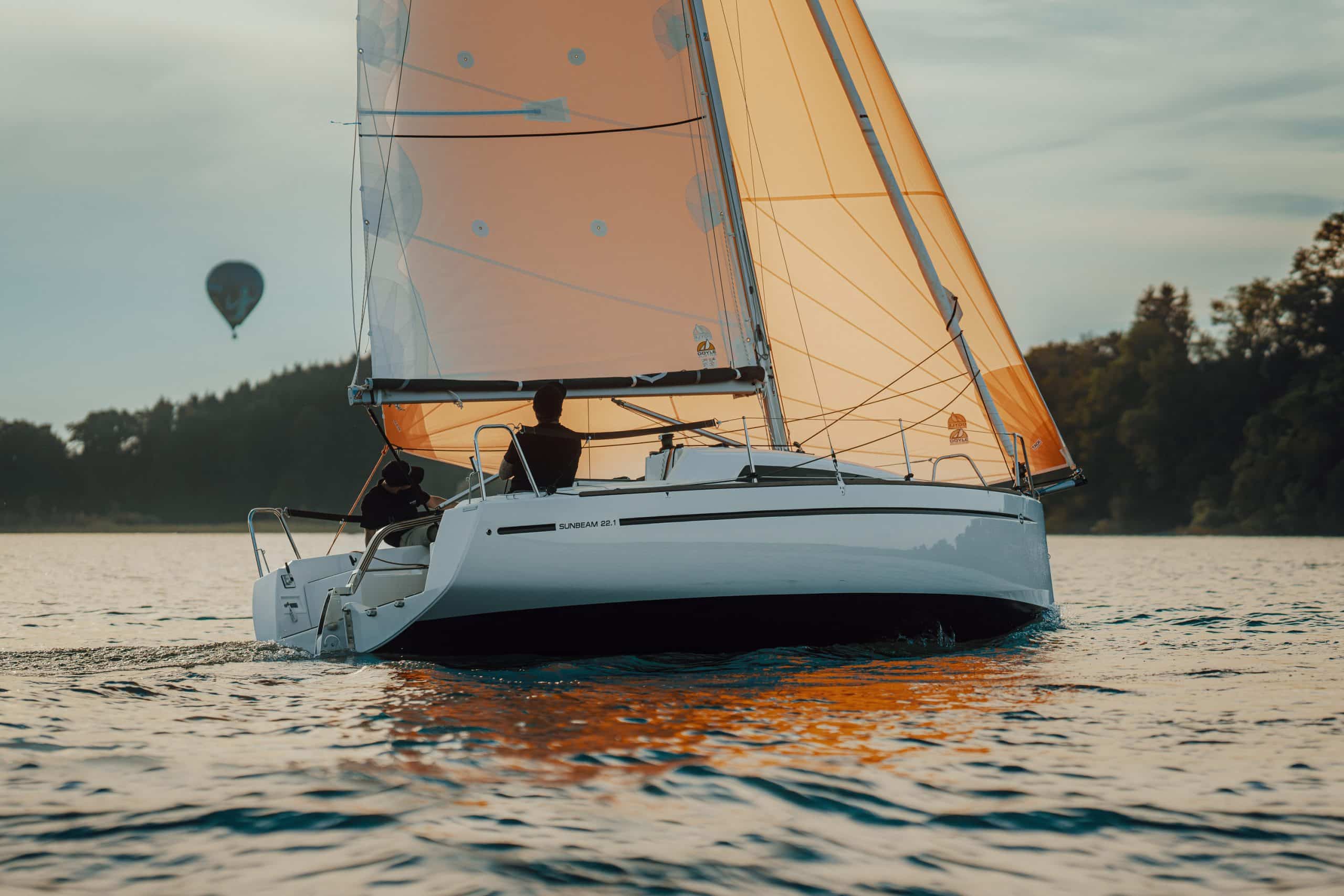 Eine Sunbeam Yacht navigiert ruhige Gewässer mit einem Heißluftballon im Hintergrund, symbolisch für ruhige und erhebende Momente