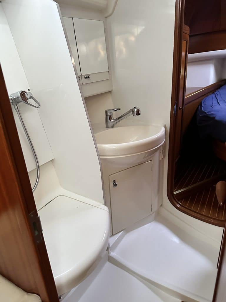 Kompaktes Badezimmer an Bord der SUNBEAM 39 mit Waschbecken, Spiegel und Toilette in Weiß, mit Holzakzenten.