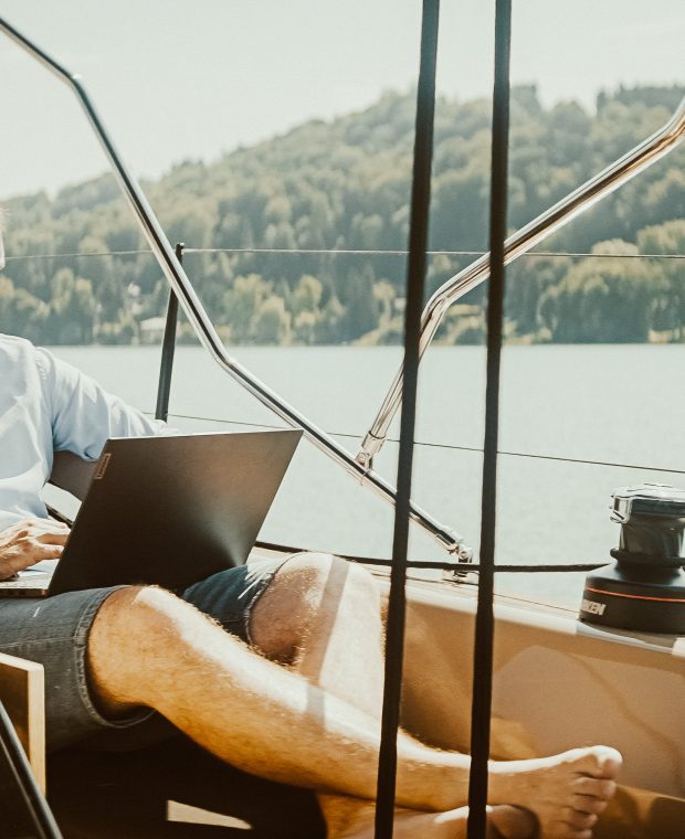 Eine Person arbeitet entspannt mit dem Laptop an Bord einer Sunbeam Yacht, umgeben von ruhigem Wasser