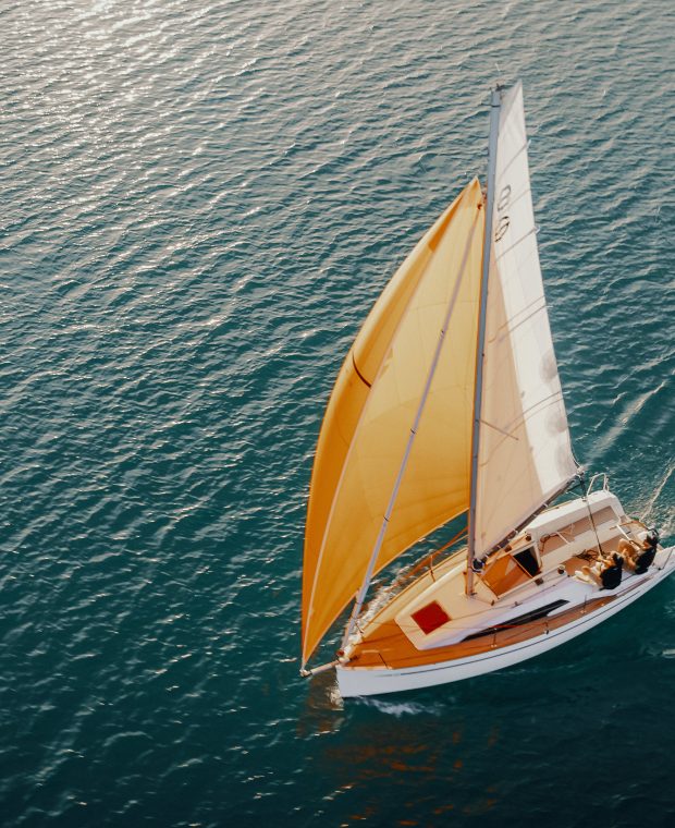 Sunbeam Yacht segelt mit geschwollenem gelbem Spinnaker auf glitzerndem Meer bei Sonnenuntergang